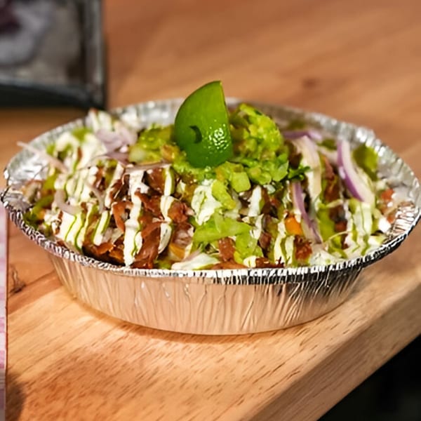 Fred's Red Tacos' Mexican food bowl with meat, lettuce, onions, sauces, guacamole, and lime.