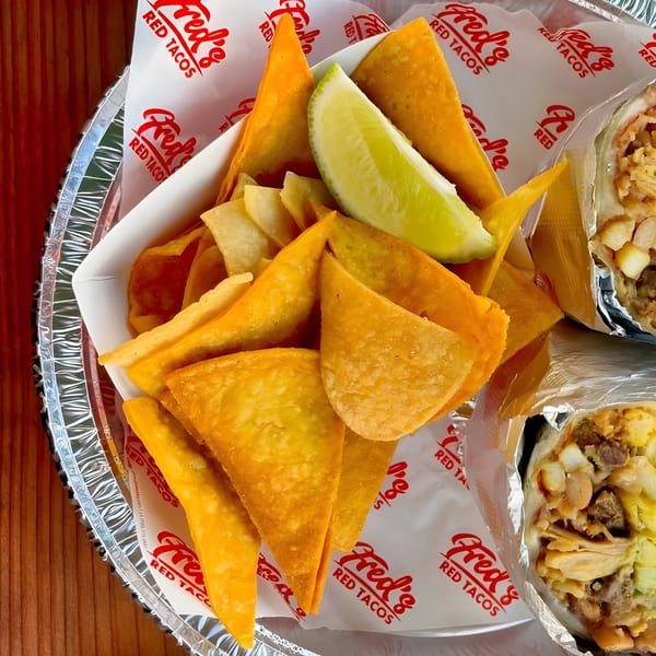Fred's Red Tacos chips with a lime wedge and burritos on a foil-lined tray.