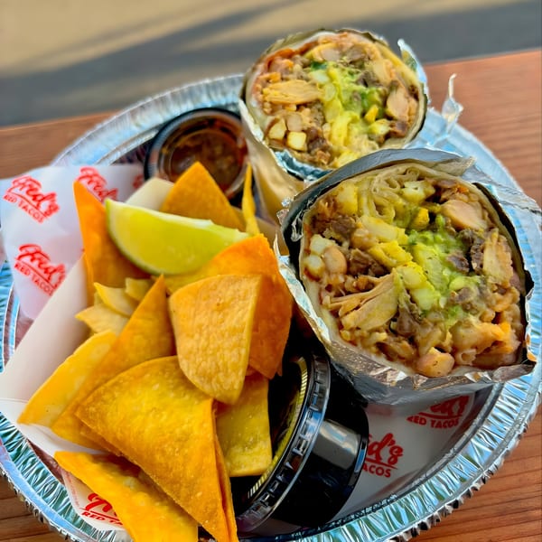 Two Fred's Red Tacos burritos and a side of tortilla chips with lime on a foil tray.