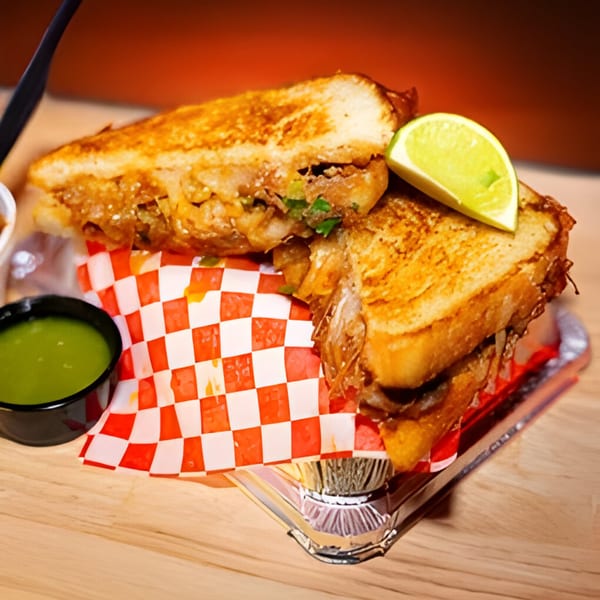 Fred's Red Tacos' grilled cheese sandwich with meat, lime, and green sauce on a wooden table.