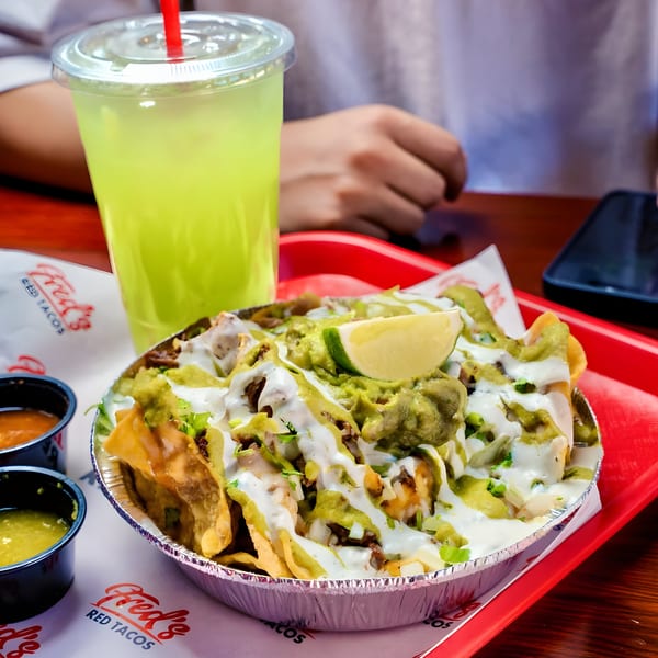 Fred's Red Tacos' loaded nachos with guacamole, sour cream, and lime, alongside a green drink.