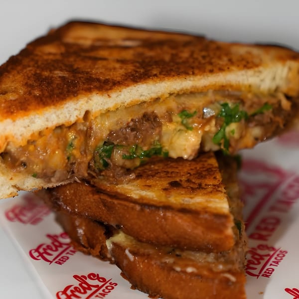 A Fred's Red Tacos grilled cheese sandwich, cut in half, revealing melted cheese and meat.