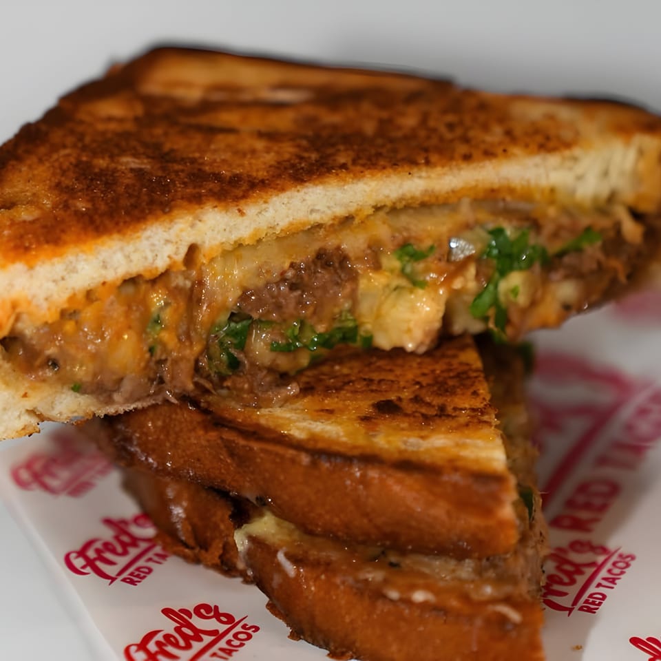 A Fred's Red Tacos grilled cheese sandwich, cut in half, revealing melted cheese and meat.