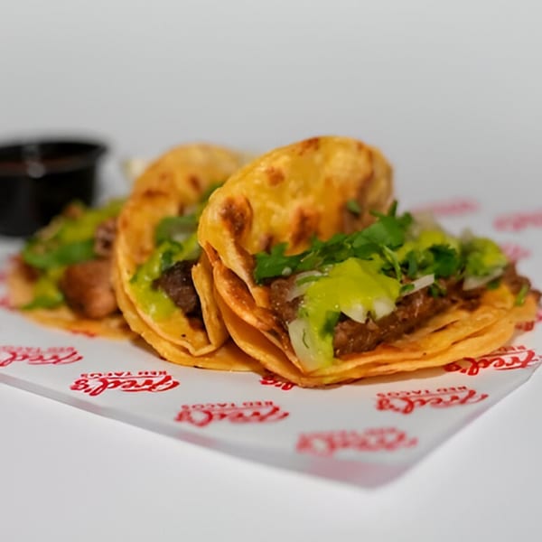 Three Fred's Red Tacos with meat, cilantro, and green sauce on branded paper.